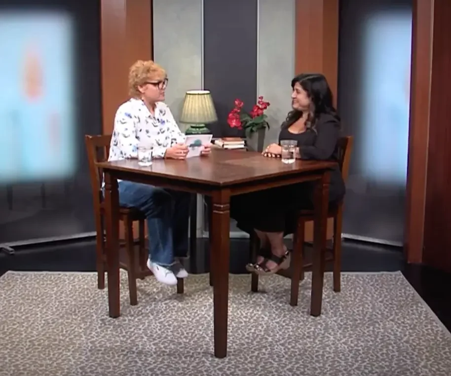 Two women sitting in a room at a table across from each other conducting an interview