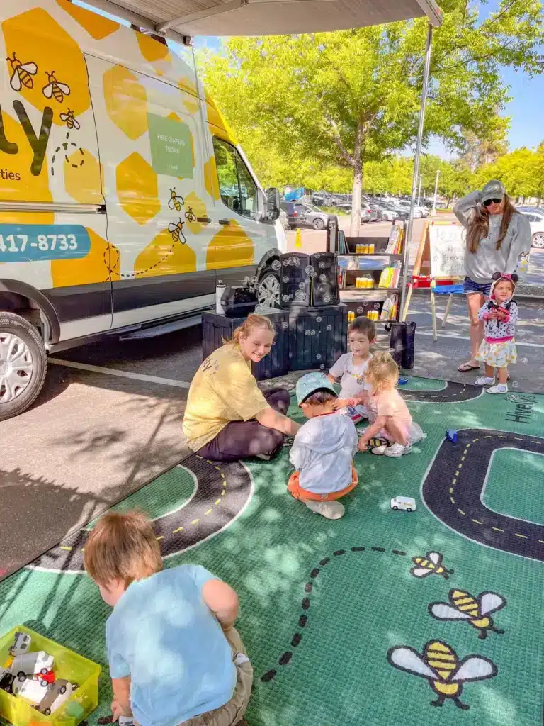 Woman sitting on a carpet with children in fron of a hively van